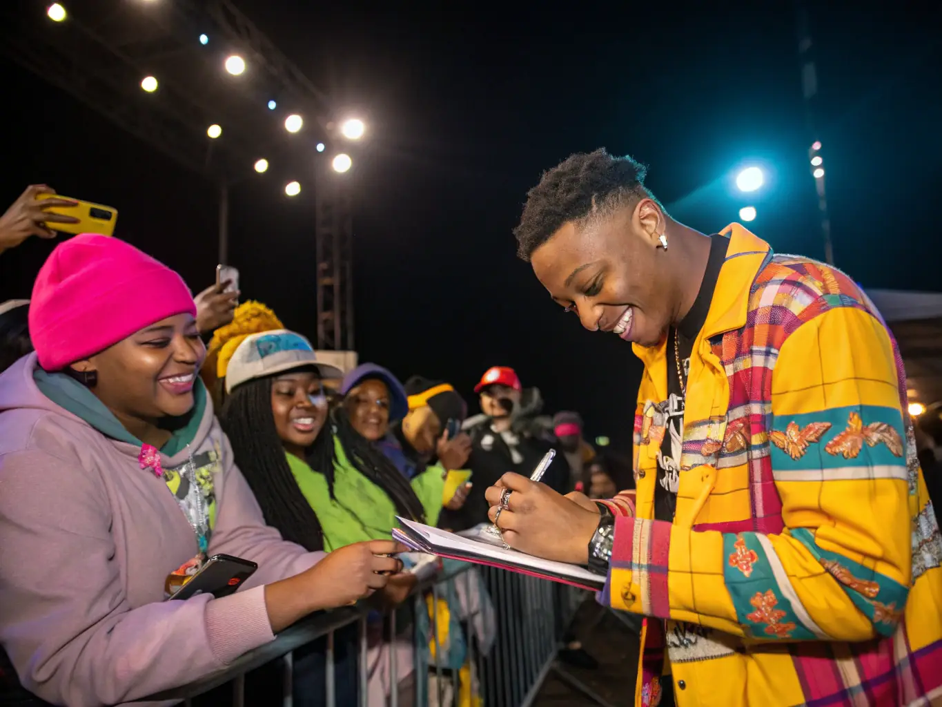 A performer is interacting with their fans after a show, signing autographs and taking photos. The crowd is enthusiastic and supportive, showing the performer's growing fanbase.